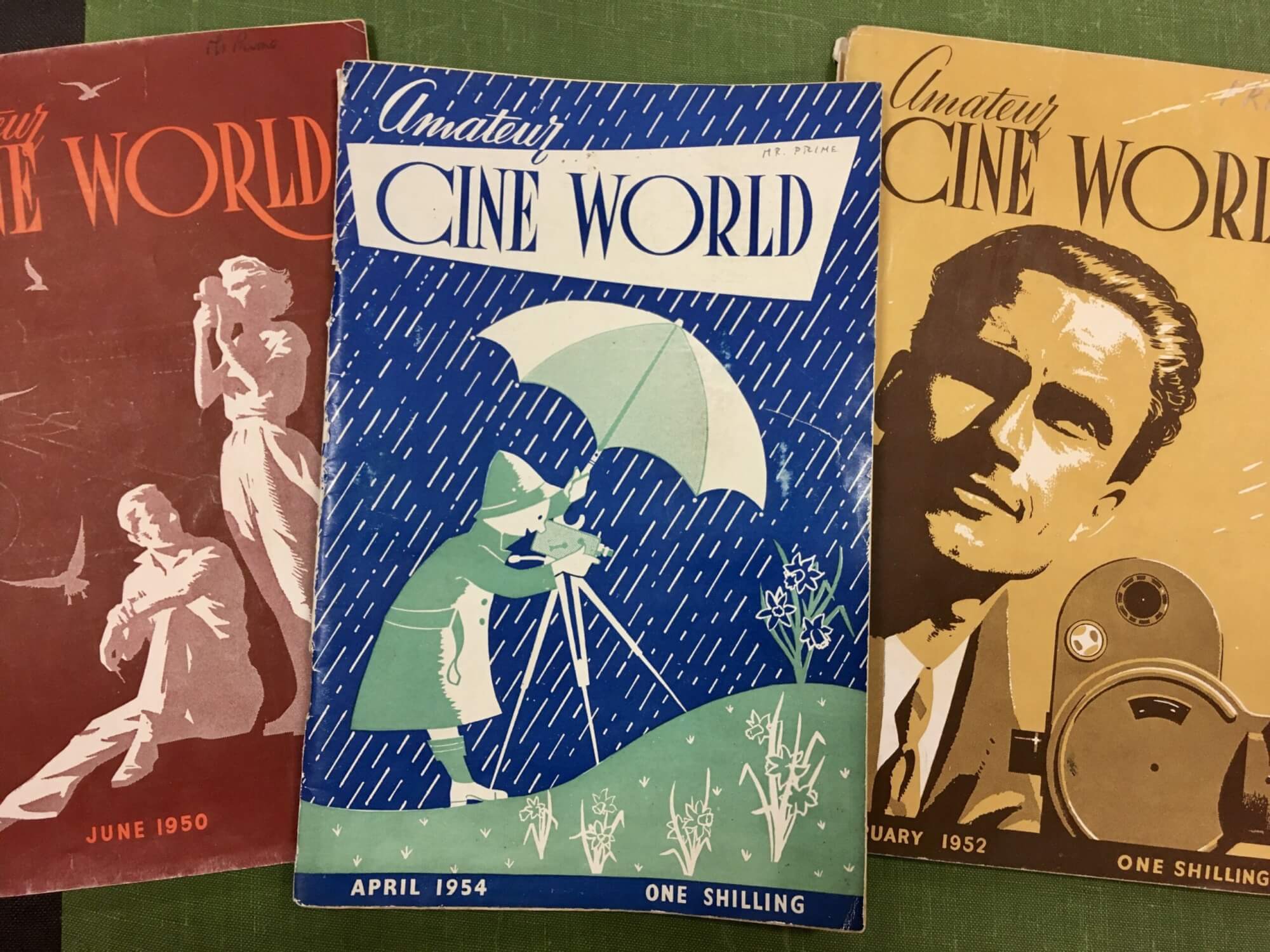 A photo showing three issues of the monthly film magazine 'Amateur Cine World' presenting the cover images showing colour illustrations of filmmakers filming with cameras.